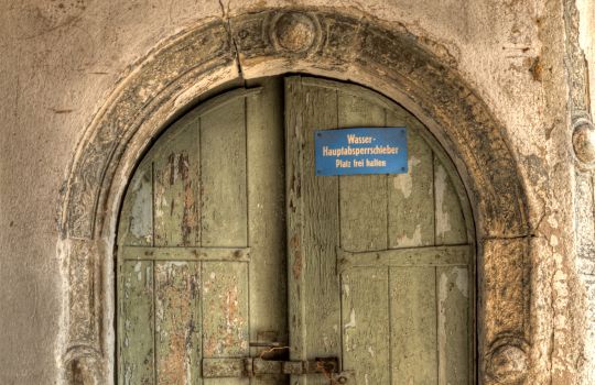 Sehr alte Holztür mit Stein und Schild.